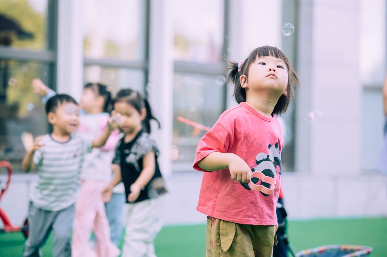 Group of children joyfully playing with bubbles in a sunny outdoor setting.