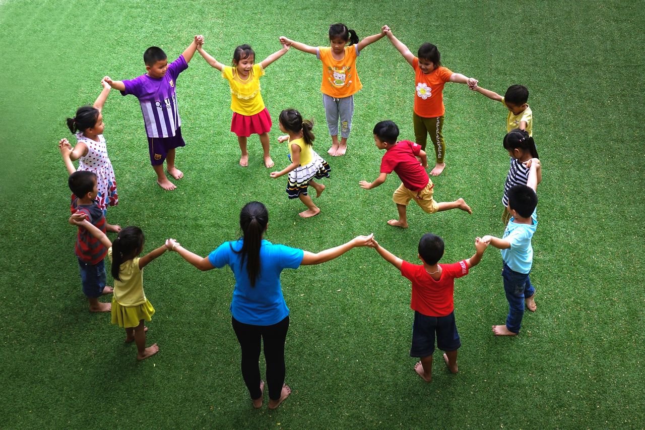 Children holding hands in a circle on green grass, engaging in a fun game outdoors.
