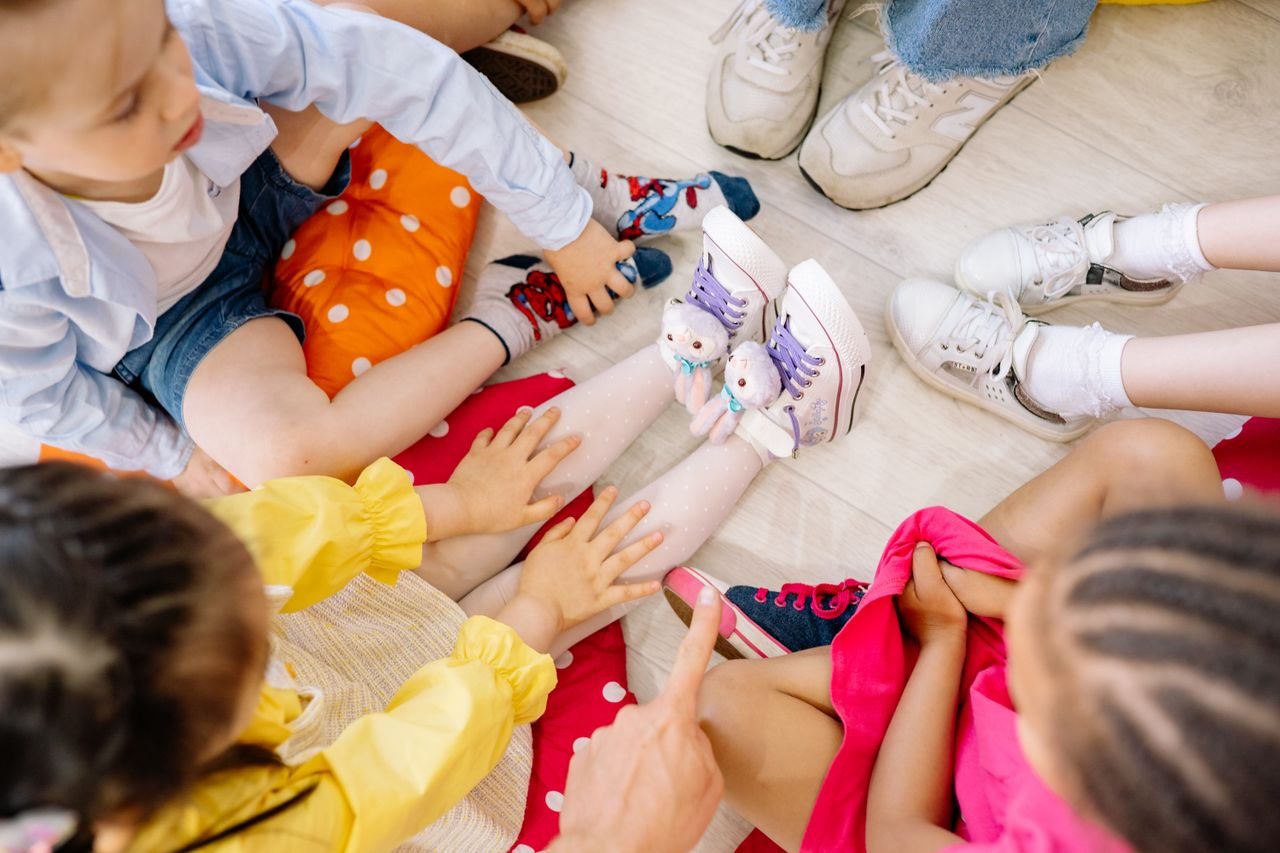 Children sitting in a circle on a wooden floor, engaging in fun indoor activities.